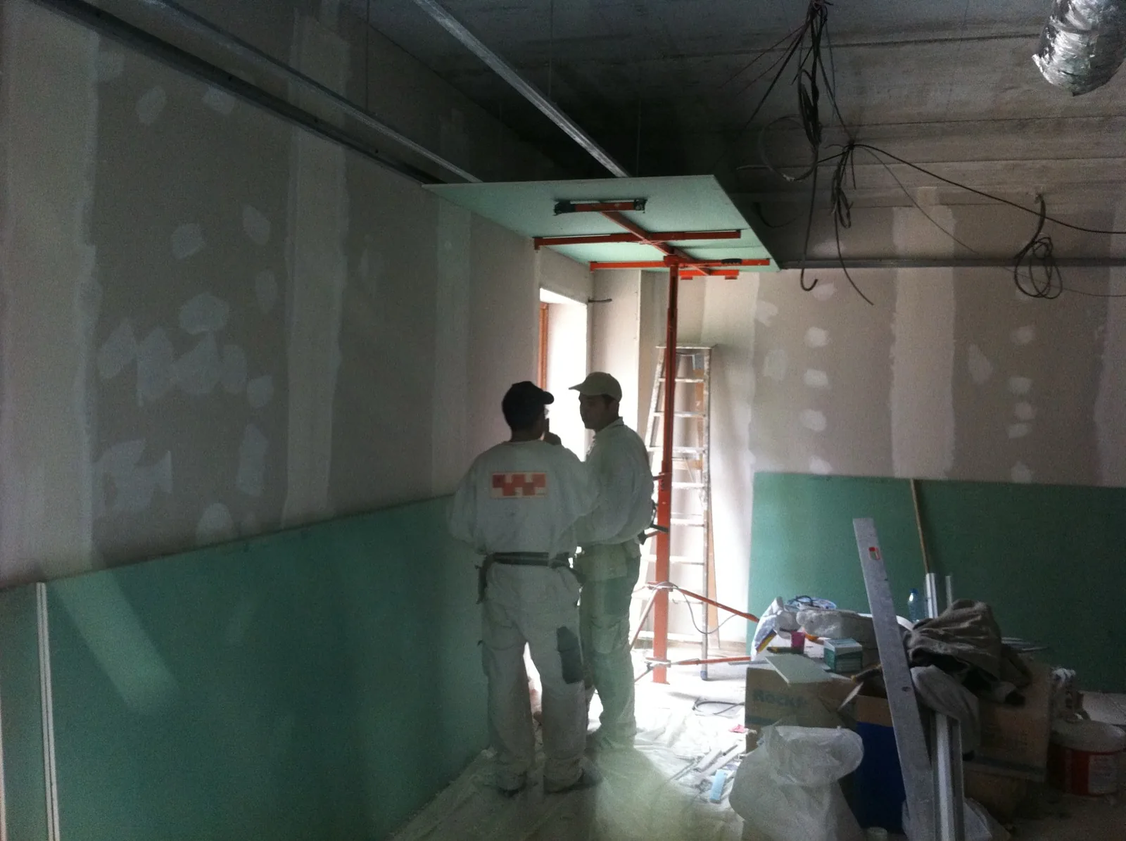 Deux compagnons Botta en tenue blanche, le damier du logo dans le dos, sur un chantier de plâtrerie en cours