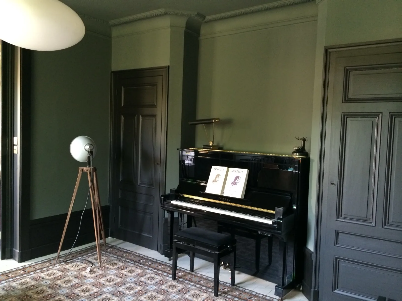 Salon d'une maison à Fourvière : murs vert sombre, portes moulurées peintes, piano droit et carreaux de ciment
